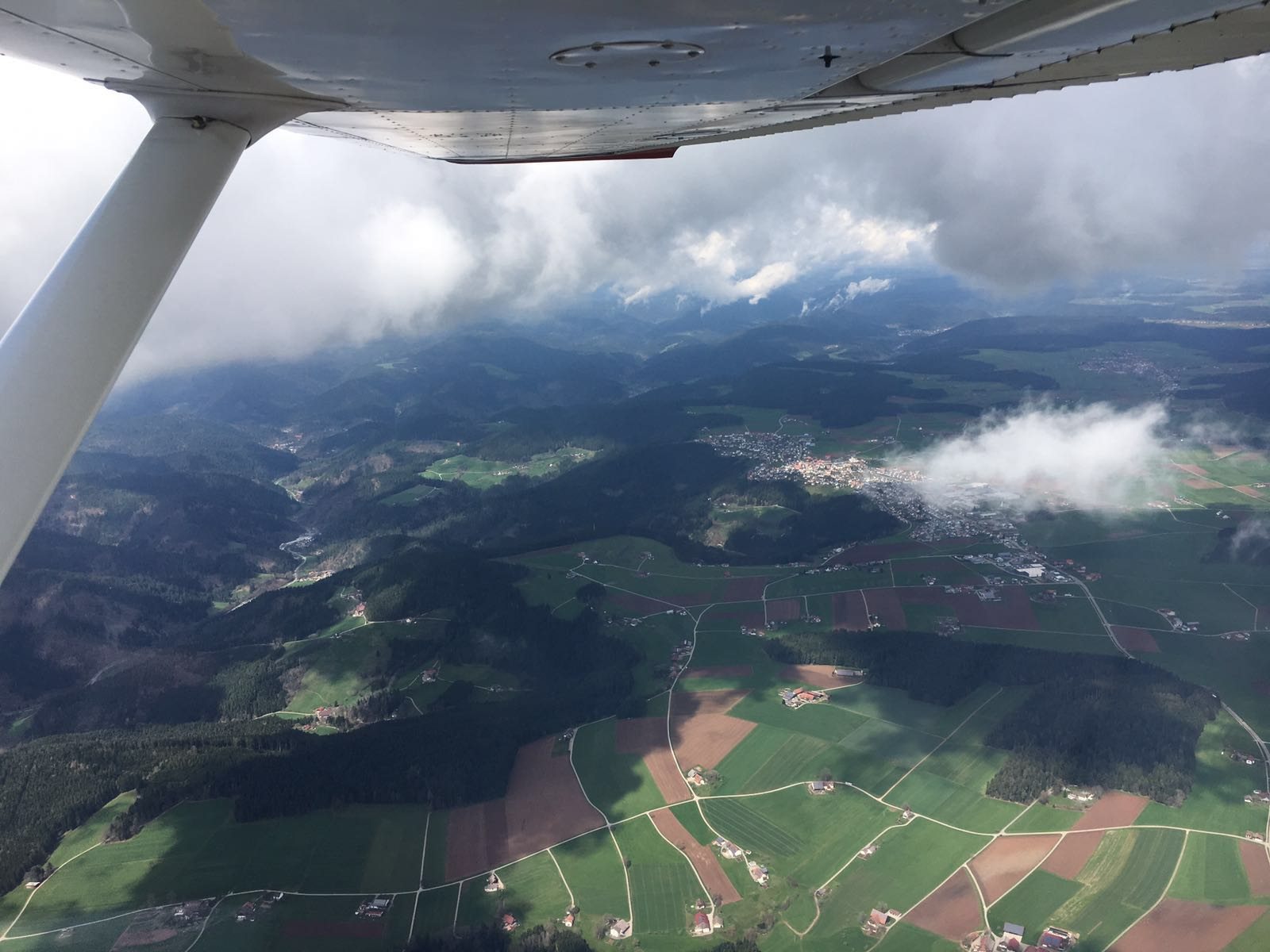Blick aus dem Cockpit auf Felder, Wald und Wolken